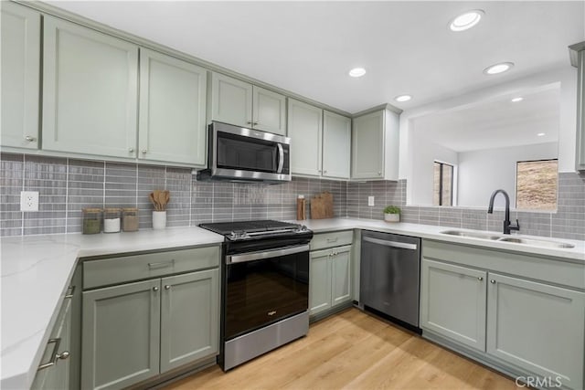 kitchen featuring a sink, light stone counters, tasteful backsplash, appliances with stainless steel finishes, and light wood finished floors