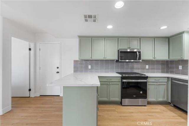 kitchen featuring light wood-type flooring, visible vents, backsplash, stainless steel appliances, and a peninsula