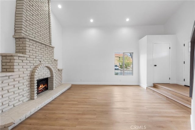 unfurnished living room featuring baseboards, a brick fireplace, and light wood-style flooring