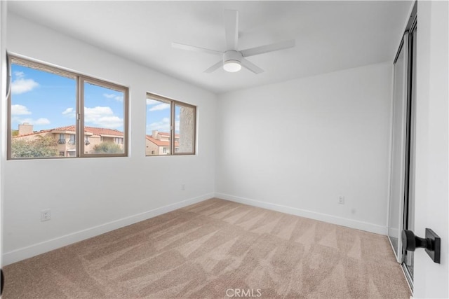 empty room with light colored carpet, baseboards, and a ceiling fan