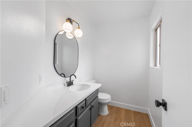 half bathroom featuring vanity, toilet, wood finished floors, and baseboards