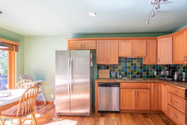 kitchen featuring decorative backsplash, appliances with stainless steel finishes, light wood-style floors, and a sink