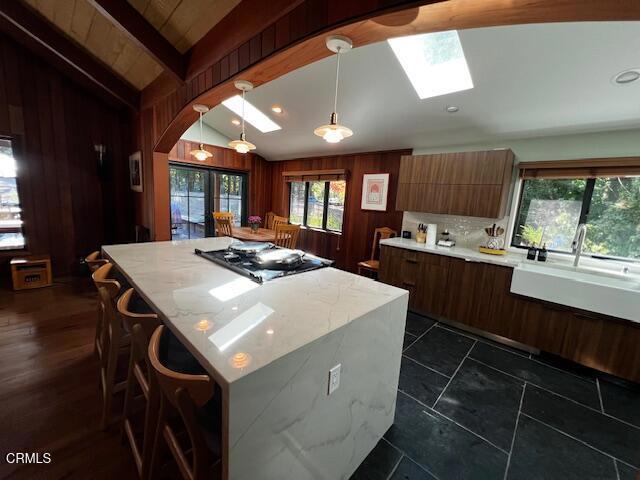 kitchen with modern cabinets, tasteful backsplash, vaulted ceiling with skylight, wood walls, and stainless steel gas cooktop