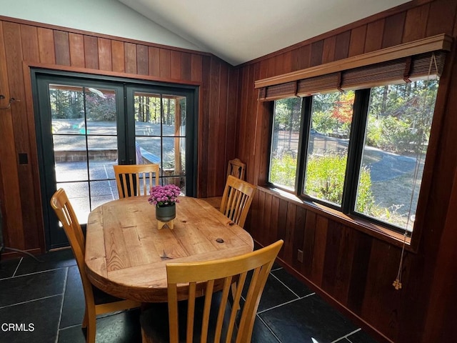 dining room with lofted ceiling, dark tile patterned flooring, and wood walls