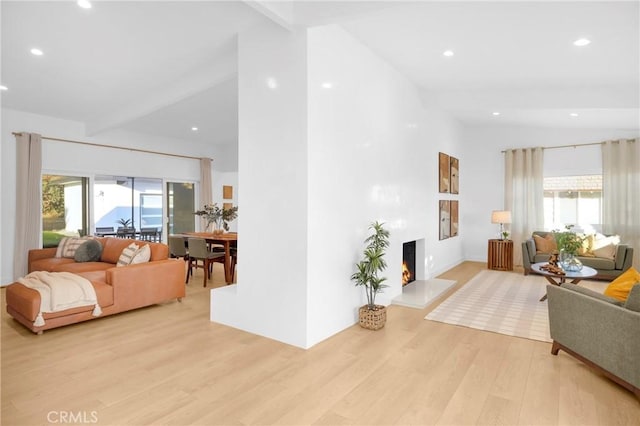 living area with light wood-type flooring, beamed ceiling, a healthy amount of sunlight, and a warm lit fireplace