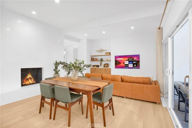 dining space featuring recessed lighting, light wood-style flooring, and a lit fireplace