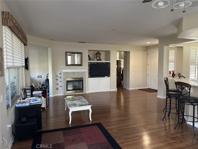 living room with built in shelves, wood finished floors, baseboards, and a tile fireplace