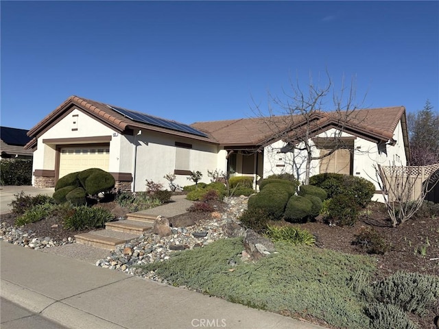 ranch-style home with stucco siding, roof mounted solar panels, a garage, and a tiled roof