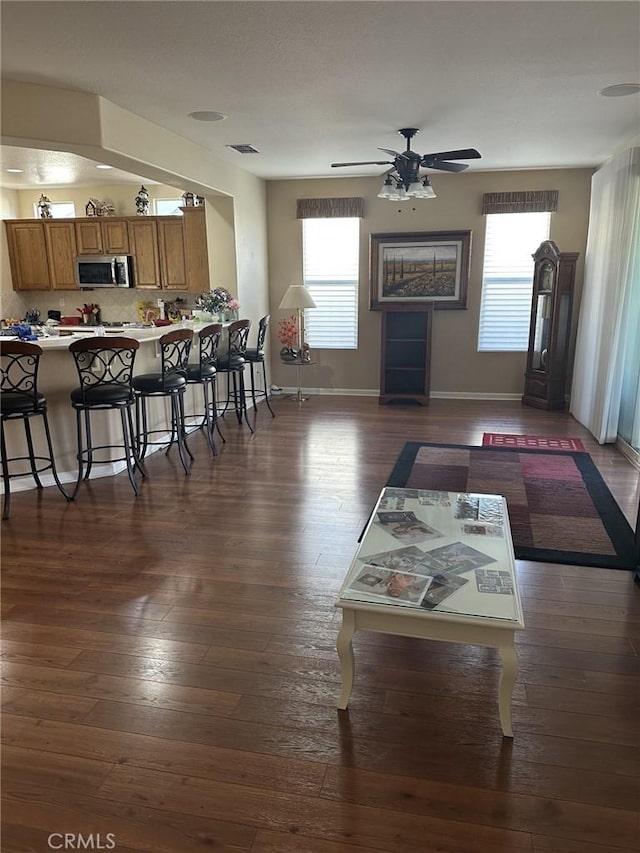 living area with dark wood finished floors, visible vents, baseboards, and ceiling fan