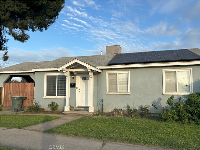 bungalow-style home with stucco siding, solar panels, a front lawn, and fence