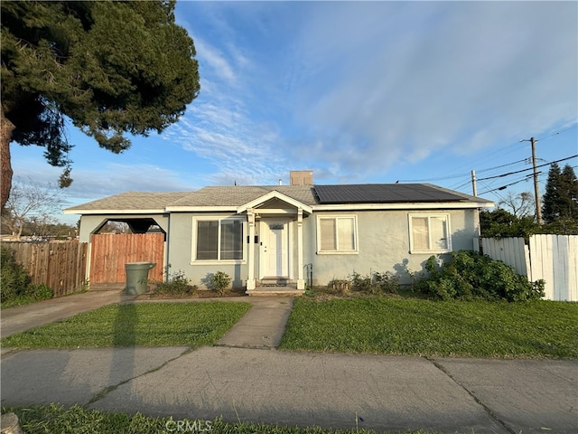 view of front of home featuring solar panels, fence, a front yard, stucco siding, and a chimney