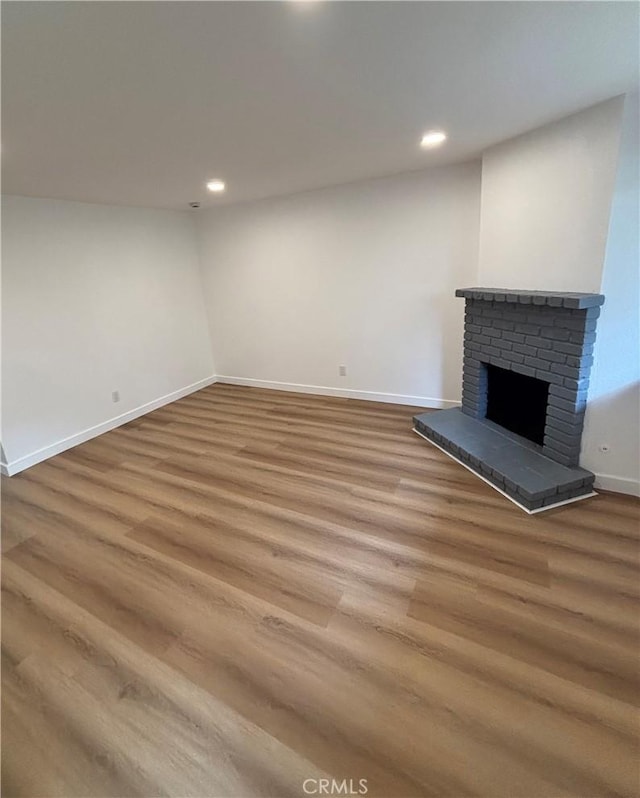 below grade area with recessed lighting, baseboards, a brick fireplace, and wood finished floors