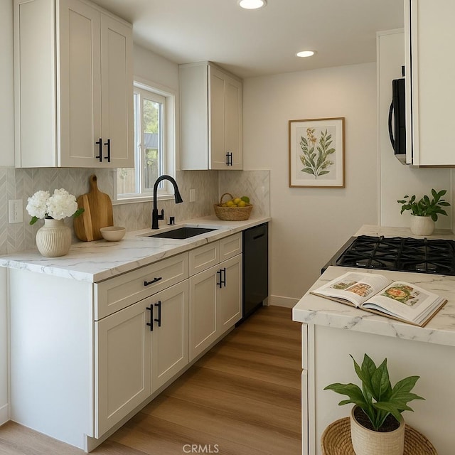 kitchen featuring a sink, black dishwasher, light wood-style flooring, tasteful backsplash, and light stone countertops
