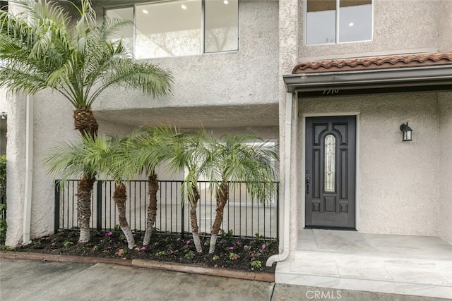 entrance to property featuring stucco siding and fence