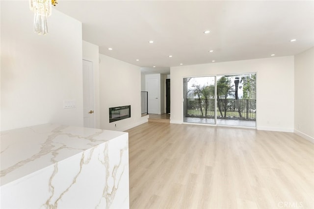 living room with a glass covered fireplace, recessed lighting, light wood-type flooring, and baseboards