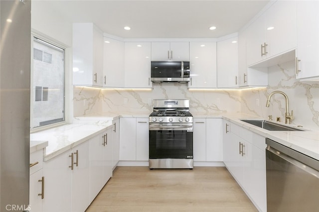 kitchen featuring light wood finished floors, light stone countertops, white cabinets, stainless steel appliances, and a sink