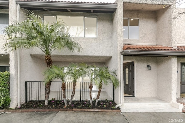 view of front facade featuring a tiled roof, fence, and stucco siding