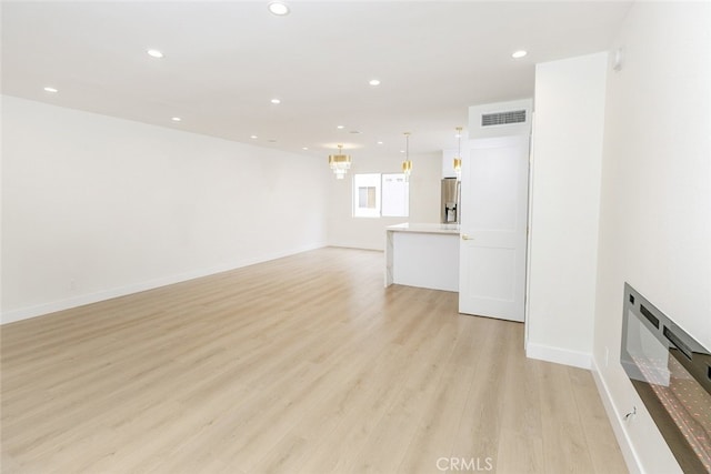 unfurnished living room with visible vents, light wood-style flooring, recessed lighting, an inviting chandelier, and baseboards