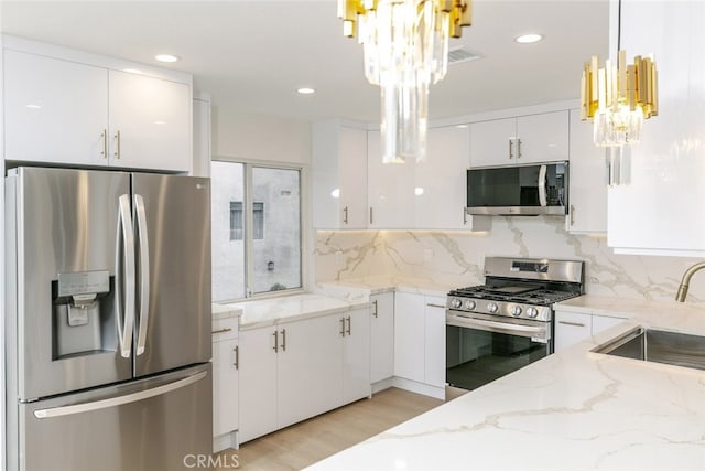 kitchen featuring light stone countertops, appliances with stainless steel finishes, an inviting chandelier, white cabinetry, and a sink