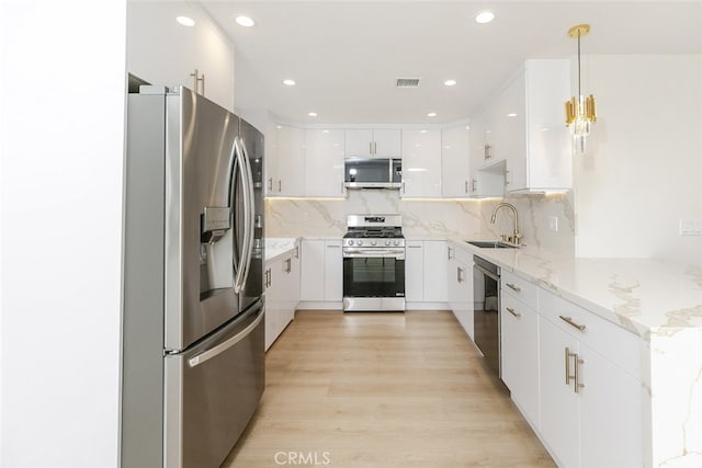 kitchen with a sink, stainless steel appliances, light wood-style floors, white cabinetry, and tasteful backsplash