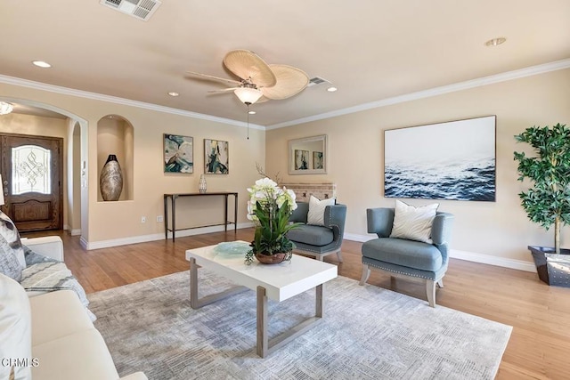 living room featuring visible vents, baseboards, ornamental molding, wood finished floors, and arched walkways