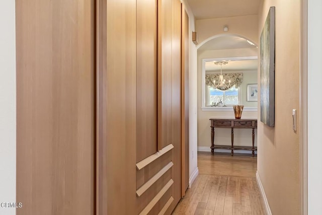 hall with a notable chandelier, baseboards, light wood-type flooring, and arched walkways