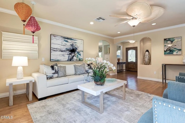 living area with visible vents, ornamental molding, wood finished floors, arched walkways, and baseboards