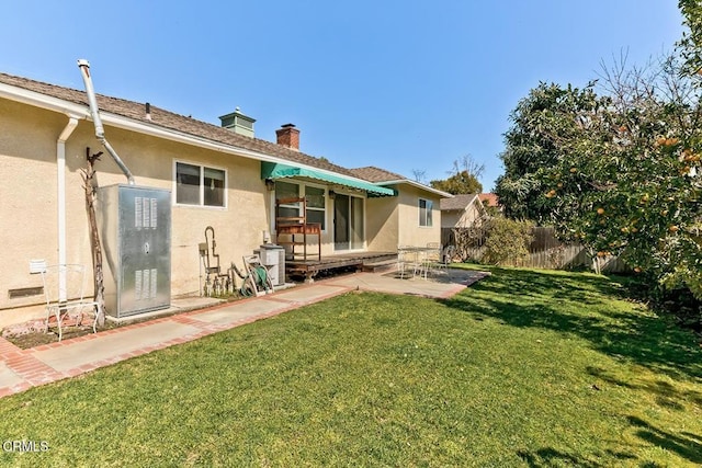 rear view of property featuring fence, a chimney, stucco siding, a patio area, and a lawn