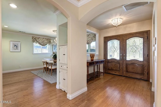 foyer entrance with baseboards, visible vents, light wood-style flooring, arched walkways, and a chandelier