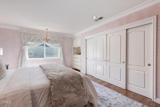 bedroom with visible vents, ornamental molding, wood finished floors, a closet, and an inviting chandelier