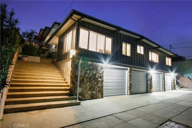 view of side of property with driveway, stone siding, stairway, board and batten siding, and an attached garage