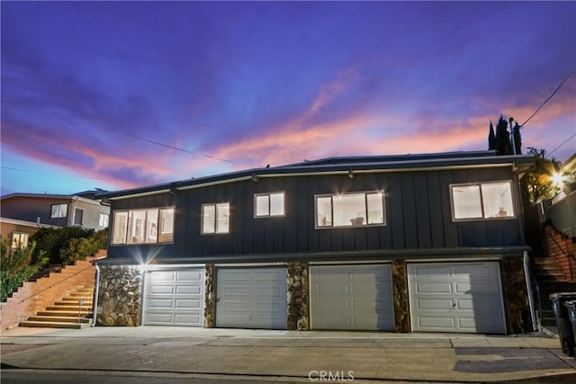 townhome / multi-family property featuring stairway, driveway, an attached garage, stone siding, and board and batten siding