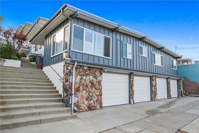 view of side of property with board and batten siding, a garage, stairs, and stone siding