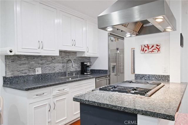 kitchen featuring stainless steel appliances, a sink, white cabinetry, wall chimney range hood, and backsplash