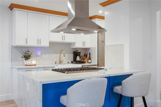 kitchen with a kitchen bar, stainless steel gas stovetop, white cabinets, and island range hood