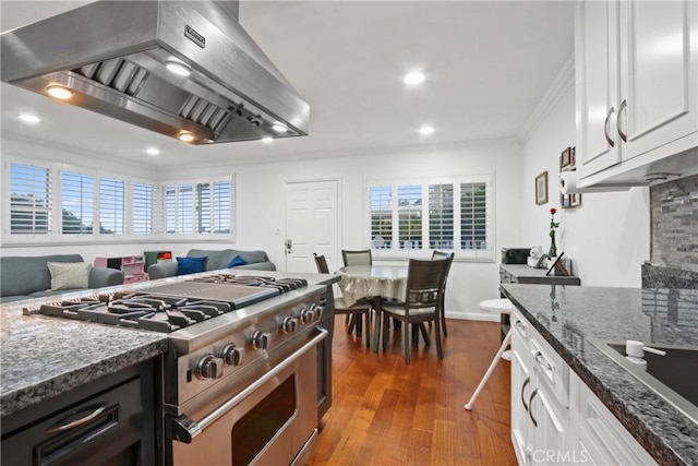 kitchen with wood finished floors, white cabinetry, high end stainless steel range oven, crown molding, and wall chimney range hood