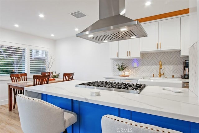 kitchen with ventilation hood, stainless steel gas cooktop, light stone counters, white cabinets, and a sink