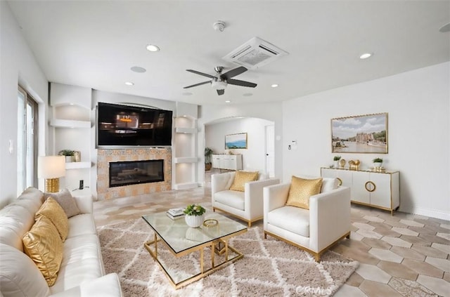 living area with built in shelves, a tiled fireplace, recessed lighting, arched walkways, and ceiling fan