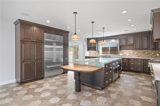 kitchen featuring dark brown cabinetry, decorative light fixtures, decorative backsplash, stainless steel appliances, and open shelves