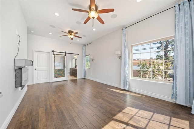 unfurnished living room with ceiling fan, a healthy amount of sunlight, a barn door, and wood finished floors