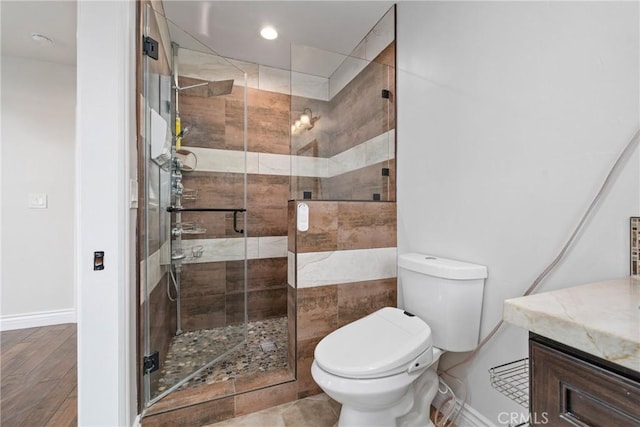 bathroom featuring a shower stall, baseboards, toilet, wood finished floors, and vanity