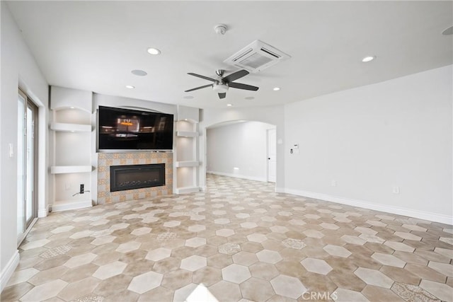 unfurnished living room featuring a ceiling fan, recessed lighting, arched walkways, baseboards, and a tile fireplace