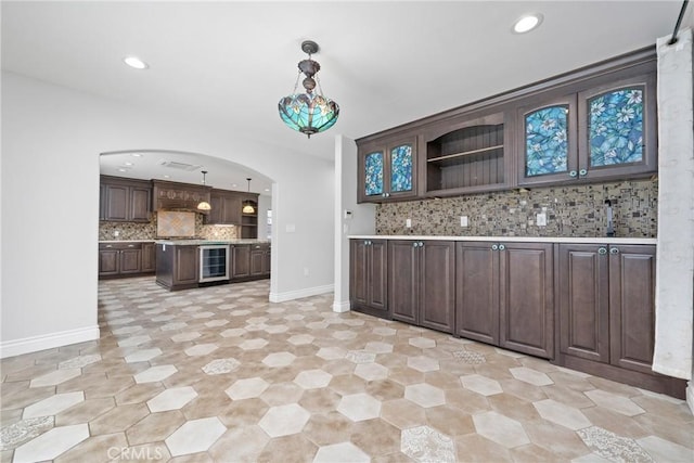 kitchen with wine cooler, arched walkways, light countertops, decorative backsplash, and dark brown cabinets