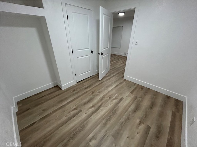 unfurnished bedroom featuring wood finished floors, baseboards, and a closet