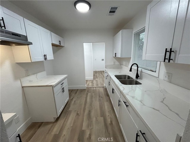 kitchen with a sink, light wood-type flooring, light stone countertops, and under cabinet range hood