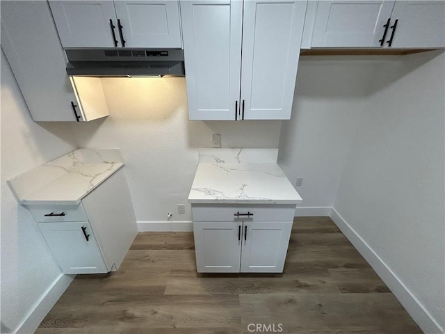 kitchen with under cabinet range hood, baseboards, light stone counters, and dark wood-style floors