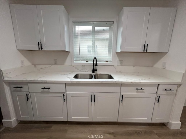 kitchen featuring a sink, wood finished floors, light stone counters, and white cabinets