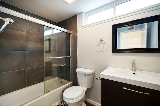 bathroom featuring visible vents, toilet, shower / bath combination with glass door, baseboards, and vanity