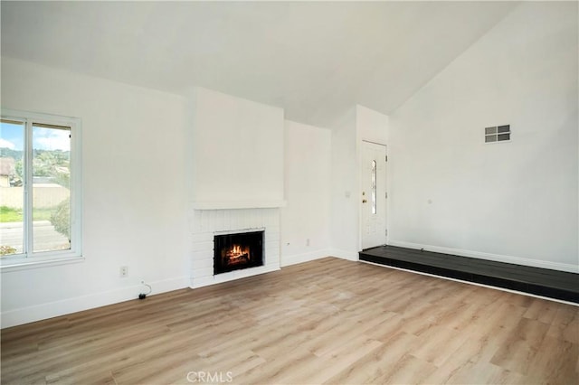 unfurnished living room with visible vents, baseboards, a brick fireplace, and light wood finished floors