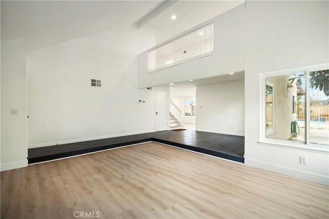 empty room featuring visible vents, high vaulted ceiling, baseboards, and wood finished floors